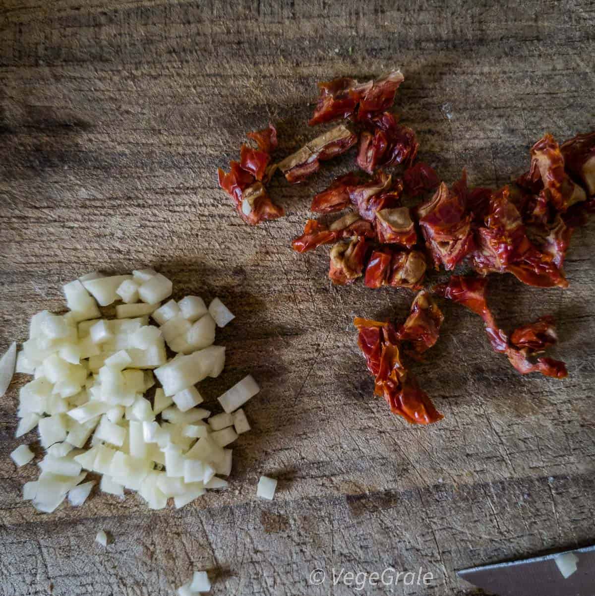 Aglio e pomodori secchi sono trittati finemente (a pochi millimetri) su un tagliere di legno vissuto.