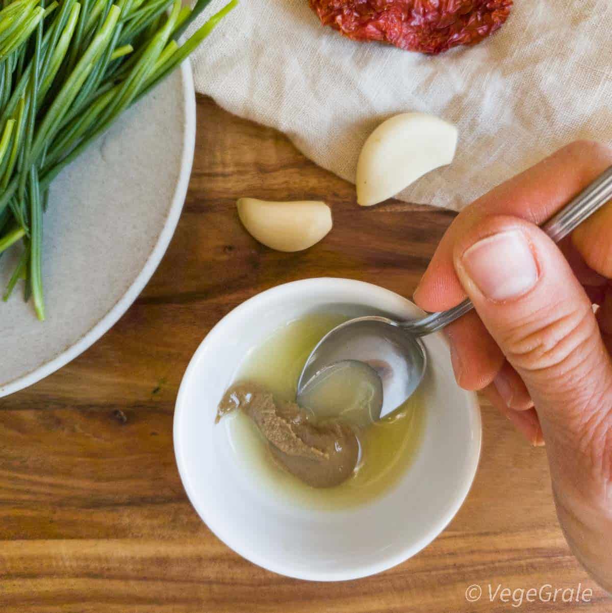 Succo di limone in una ciotolina bianca con un cucchiaino di tahina ancora non mischiati. Si vede la mano con il cucchiaino che sta per mischiare.