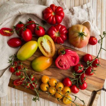 Grande varietà di pomodori da insalata estivi disposti su un tavolo e tagliere. Pomodoro cuore di bue, ciliegini gialli e rossi, datterini, riccio nostrano, ovale verde, e picadilly pixel.
