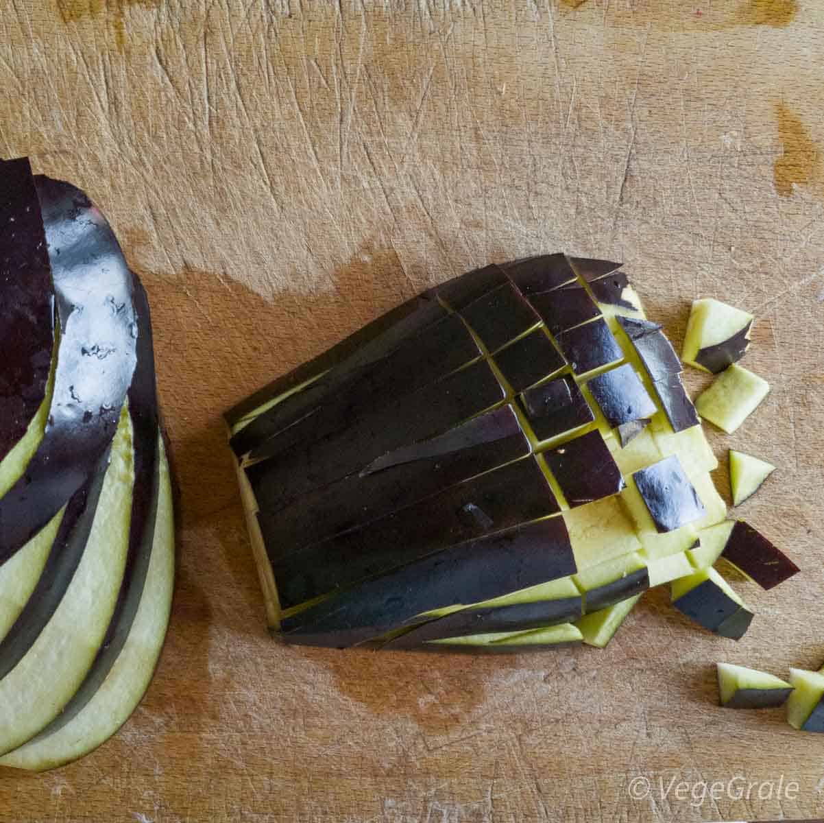 melanzana tagliata su tagliere. sulla sinistra solo tagliata a fette di 1-2 centimetri, sulla destra tagliata anche di traverso per formare cubetti.