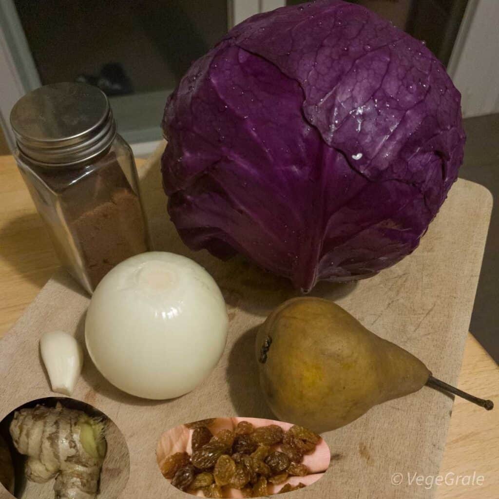 un cavolo rosso, cipolla pulita, spicchio d'aglio pulito, pera, zenzero, uvetta e polvere di chiodi di garofano su tagliere.