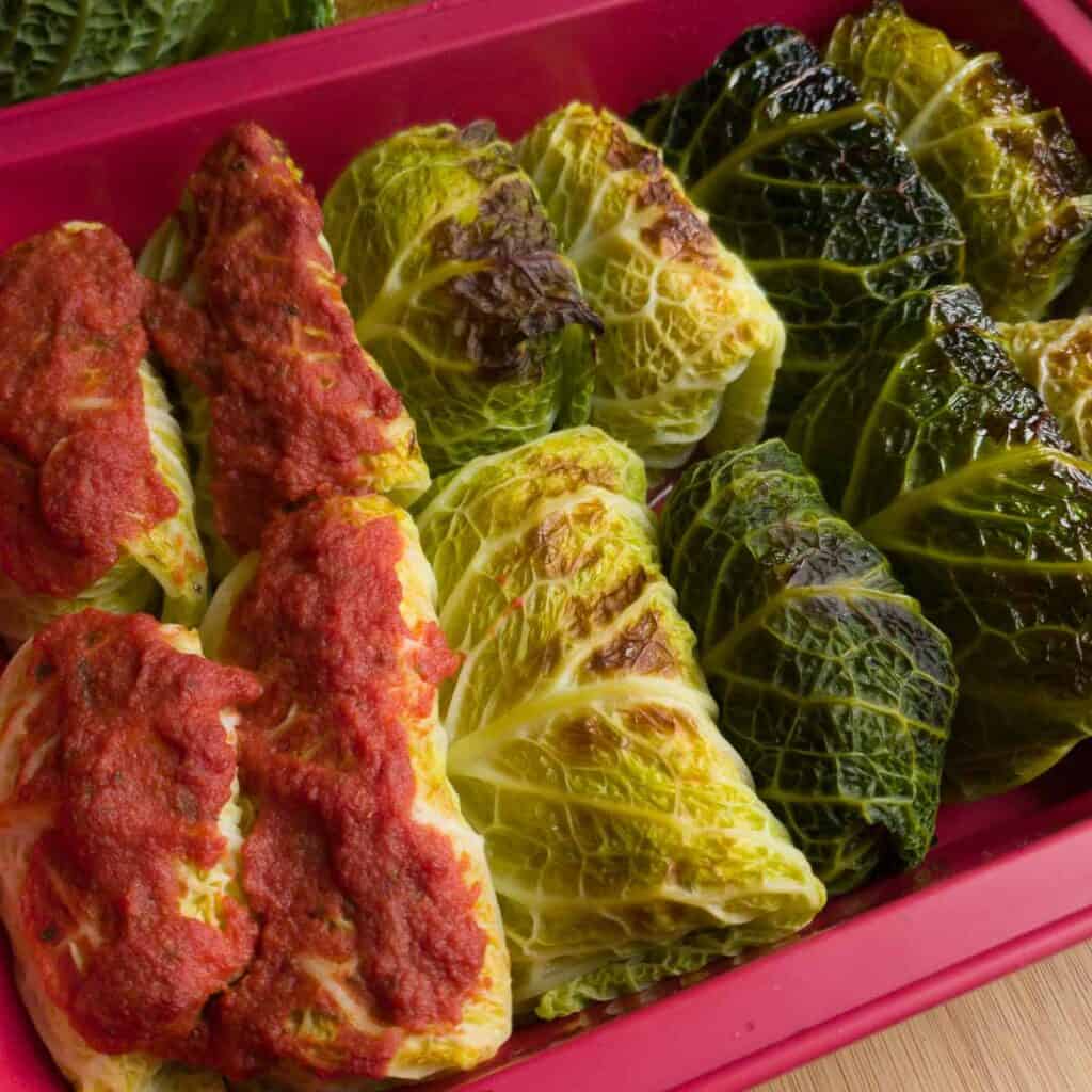 Involtini di verza vegani cotti in forno con diverse opzioni di topping: Su una parte pomodoro sopra, su una parte niente sopra, su una parte olio sopra.