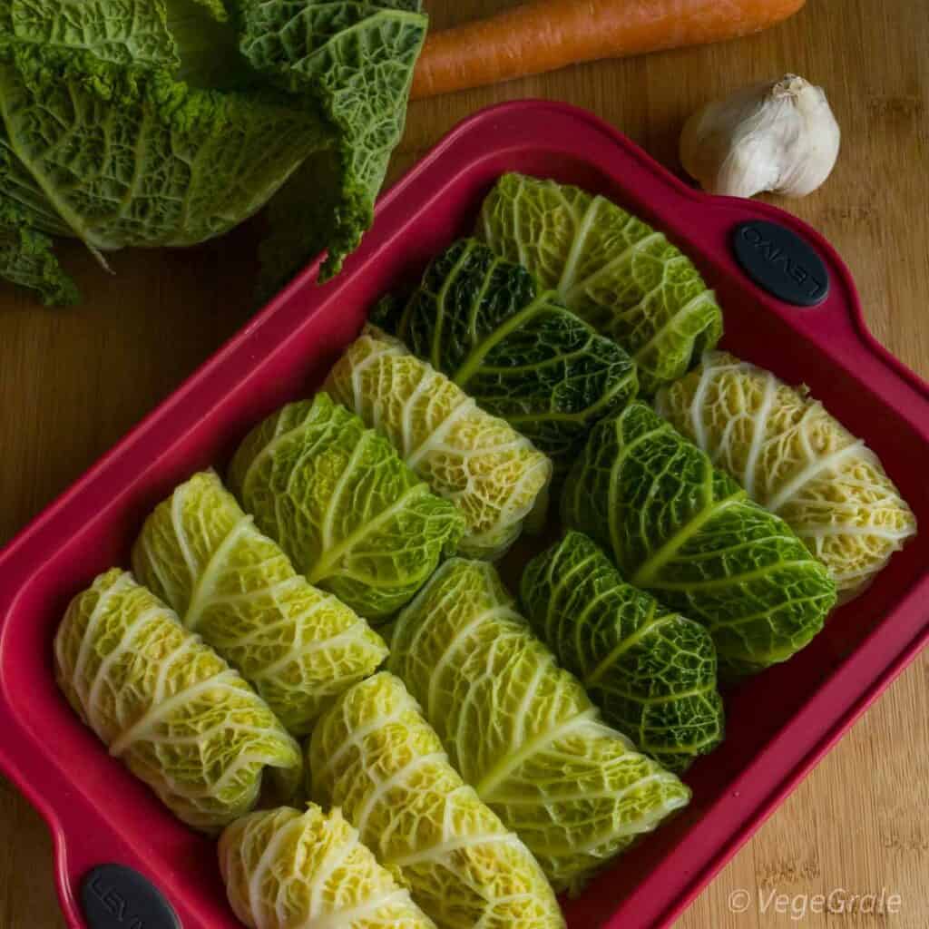 Involtini pronti per essere cotti disposti in due righe in una teglia da forno rossa in silicone.