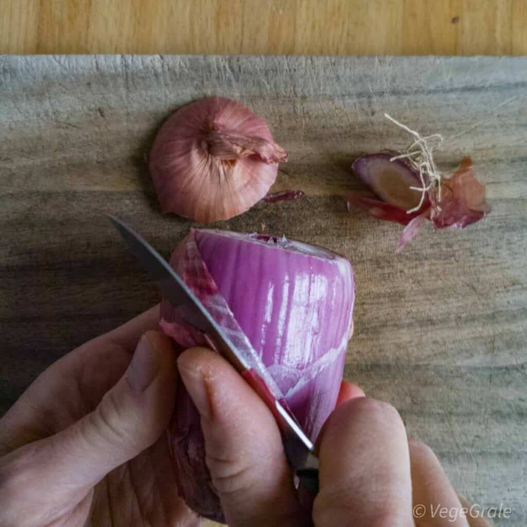 Le due estremità della cipolla sono già state tagliate via e poggiano sul tagliere. Ora vengono rimossi i strati più secchi esterni della cipolla.